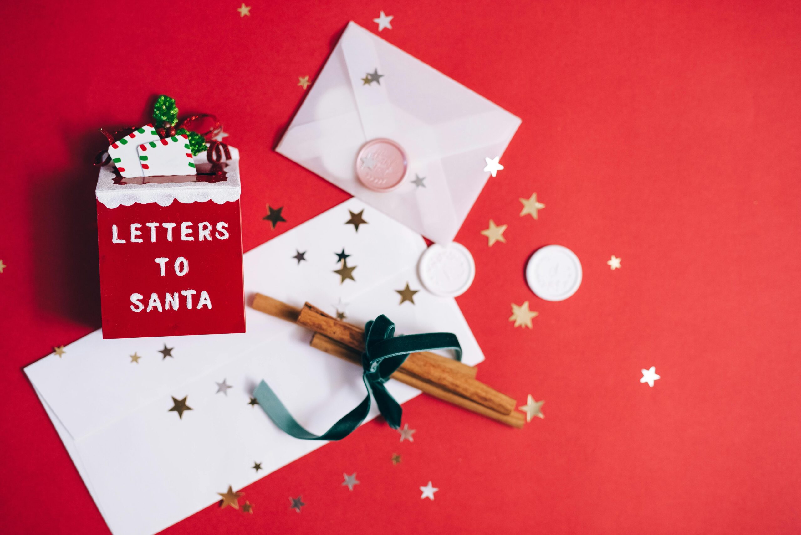 A festive flatlay with letters to Santa, envelopes, and holiday decorations on a red background.
